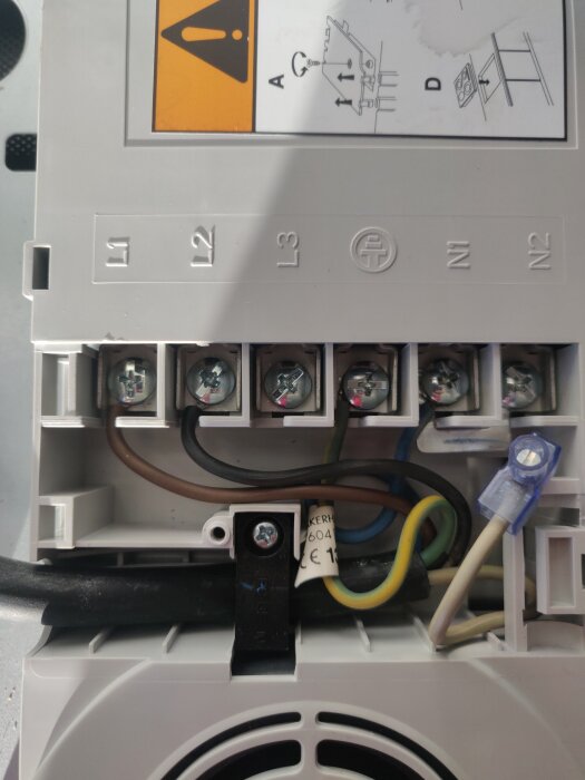 Elinstallation med bruna, svarta, och gröna kablar anslutna till L1, L2, och jord på en kopplingsplint, detaljerat schema synligt ovanför.