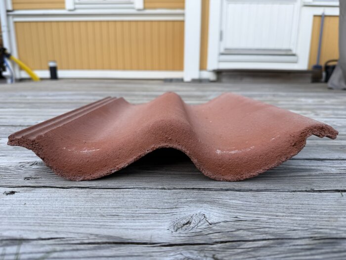 Tegelröd Zanda takpanna av typen Aerlox på en träyta, visar pannans form och färg i närbild.