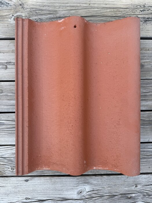 Tegelröd Zanda takpanna på en träyta, fokus på formen och färgen.