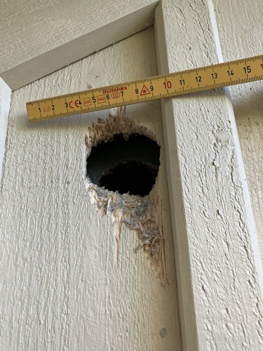 Hål i träfasad med synlig isolering och ett måttband.