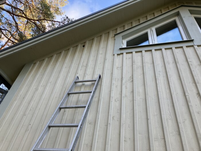 Nybyggt hus med träfasad och en stege lutad mot väggen. Ett hål syns högst upp vid taket nära fönstret.