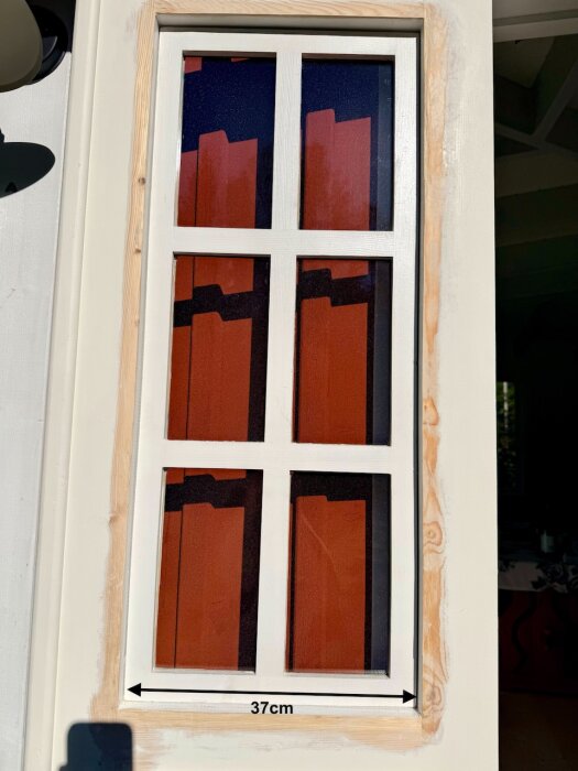 En vitmålad fönsterbåge med glasrutor, delvis borttagen kitt, och en mätt linje som visar bredden 37 cm, röd vägg i bakgrunden.