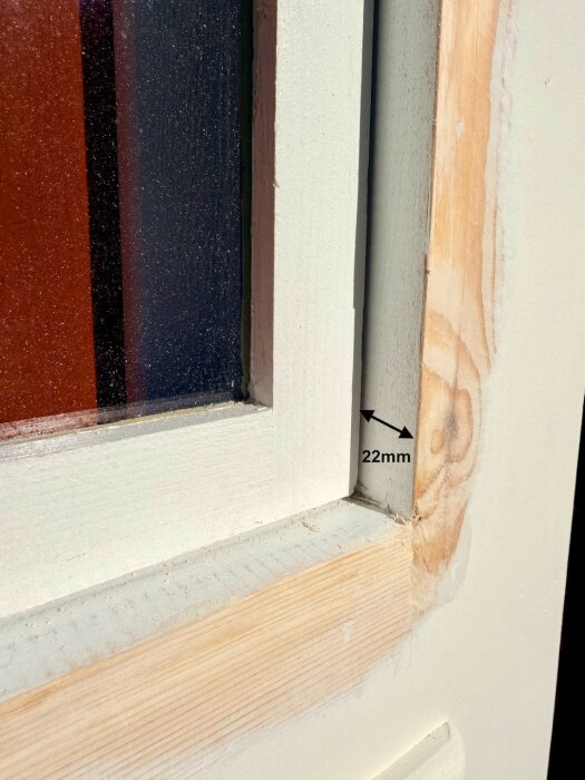 Närbild av ett fönster där en träinramning visar djupet 22mm, vilket är markerat med en pil och text.