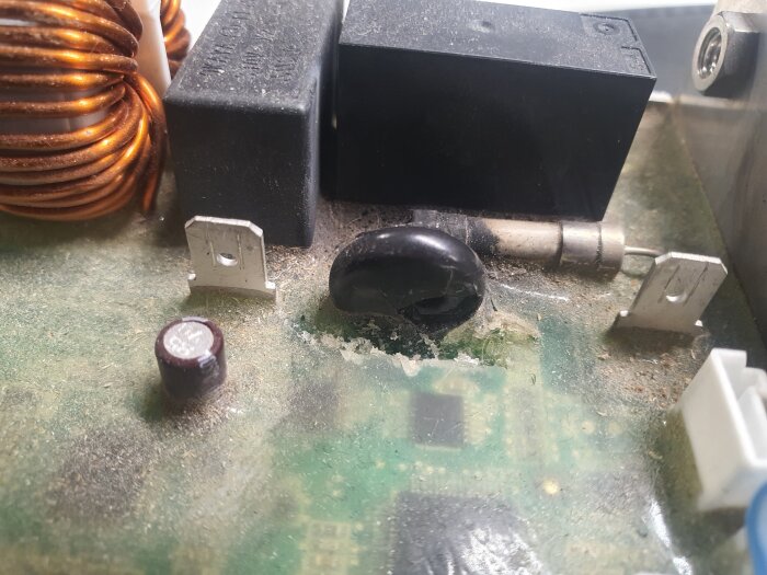 Detalj av elektronisk kretskort med brända komponenter, kopparspole och skadade säkringar i en kompressor.