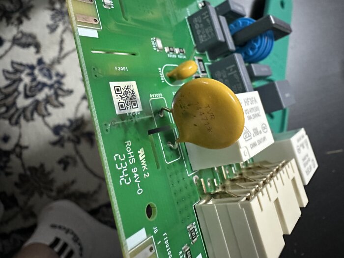 Kretskort med flera komponenter inklusive en gul TVR 14471 MOV, missfärgad fläck bredvid den, potentiell orsak till värmeproblem i diskmaskin.