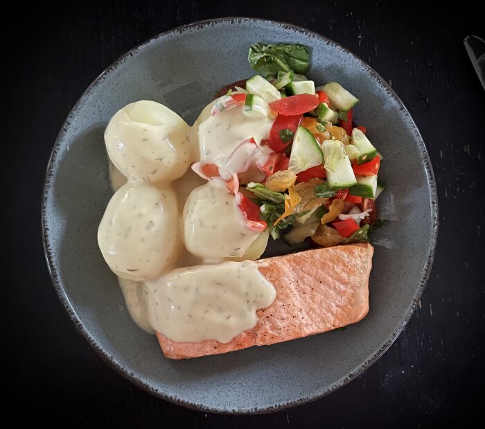 Stekt lax med kokt potatis, sallad, täckt med citron- och dillsås på en grå tallrik.