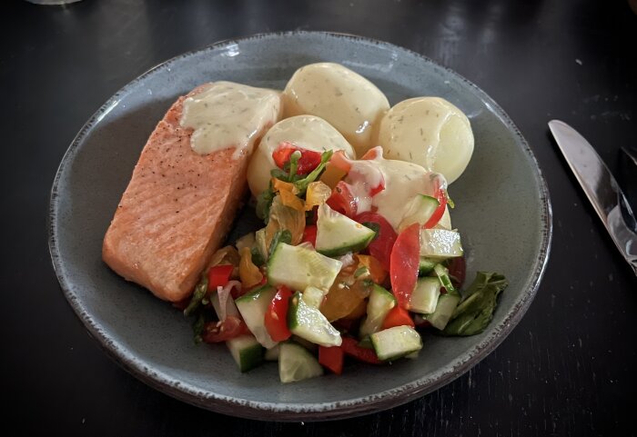 Tallrik med stekt lax, kokt potatis, sallad och citron- och dillsås.