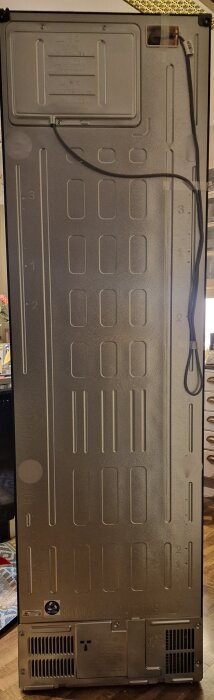 Baksidan av kyl/frysskåp utan luftspalt, med ventilationsgaller längst ner och elsladd till höger.