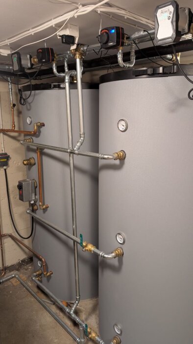 Två stora ackumulatortankar med rördragning i en källare, flera cirkulationspumpar och mätare installerade ovanpå tankarna.