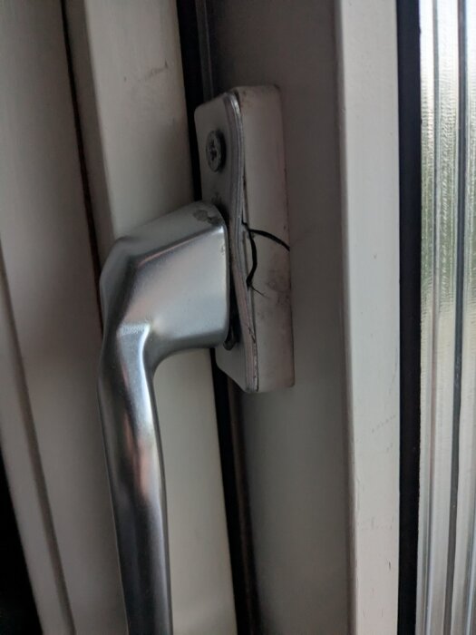 Sprucket altandörrshandtag i metall, delvis lossnat från dörren.