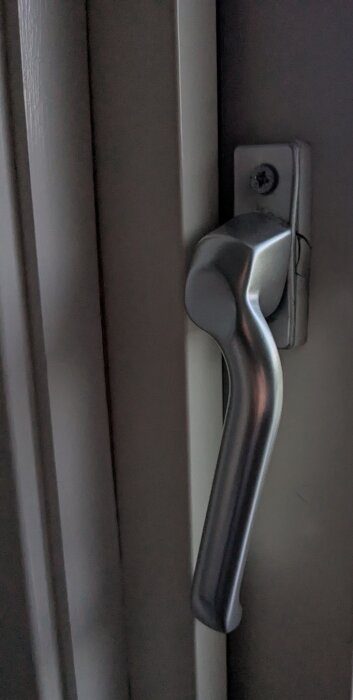 Trasigt dörrhandtag av metall på altandörr, skruvfäste synligt.