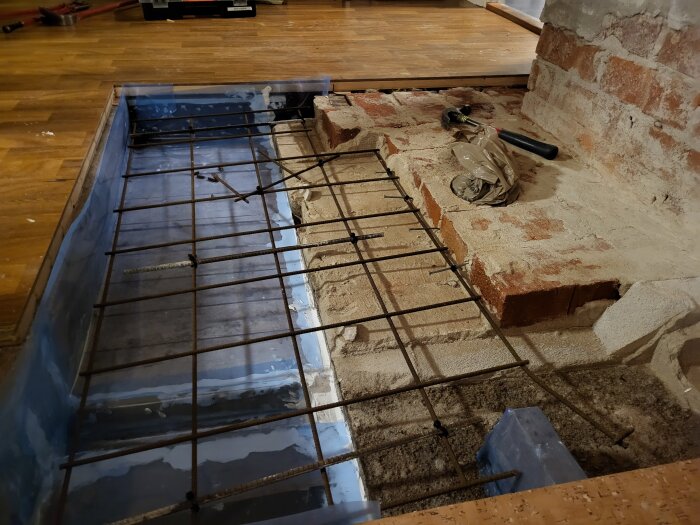 Byggprojekt med armeringsjärn över blå grund och tegelmur; pågående renovering.