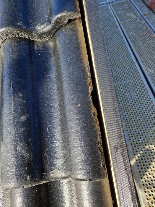 Takpanna på 70-talsvilla med liten defekt vid kanten, nära en takränna. Panelen intill är blöt. Byggnadsställning i bakgrunden.