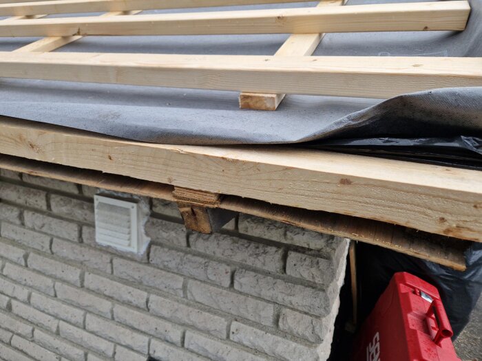 Närbild av hustak med trä- och plywooddetaljer, takfotsbrädor och diffusionsduk ovan murad fasad.