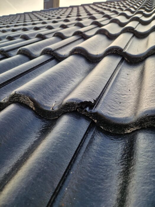 Närbild på ett tak med svarta takpannor, där en panna har en mindre skada längs kanten.