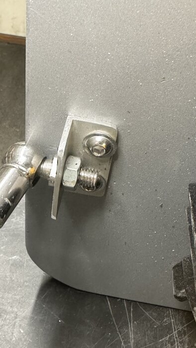 Närbild på en metallfäste till ett justerbart extrabord, med bult och mutterfäste på slipmaskinens sida.