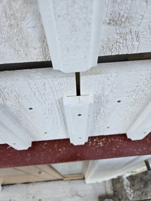 Vit träpanel på husfasad med sprickor och mindre hål.