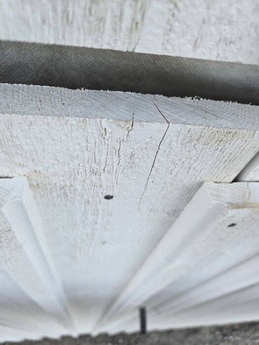 Sprickor och små hål i vit träfasad på ett nybyggt hus, närbild tagen av husägare för bedömning.