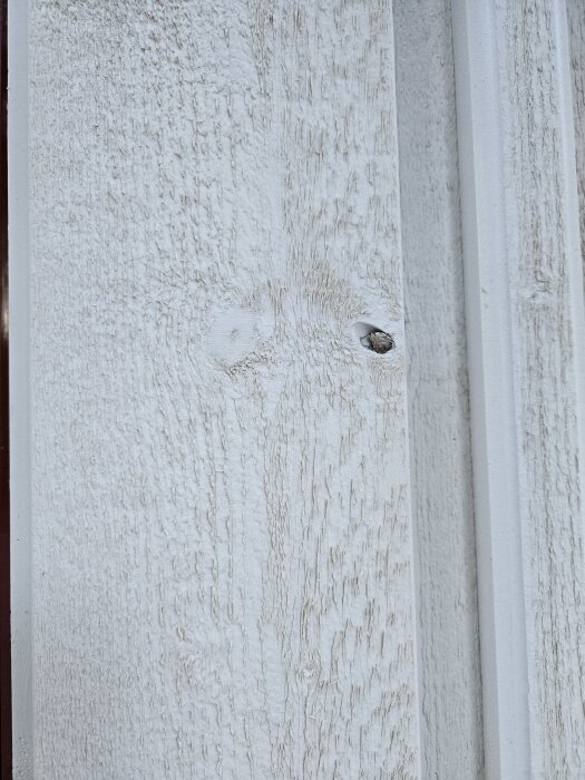 Fasad med vit träpanel som visar små sprickor och ett hål i ytan.