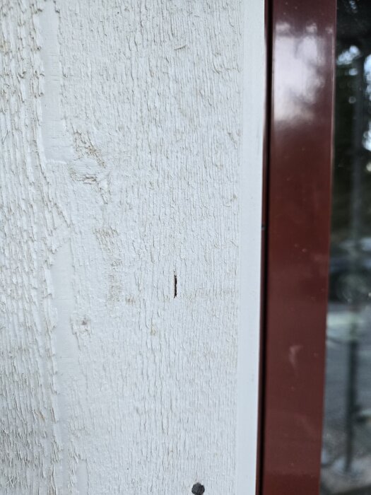 Fasad med en liten spricka nära en brun fönsterkarm, texturen är grov och ytan vitmålad.