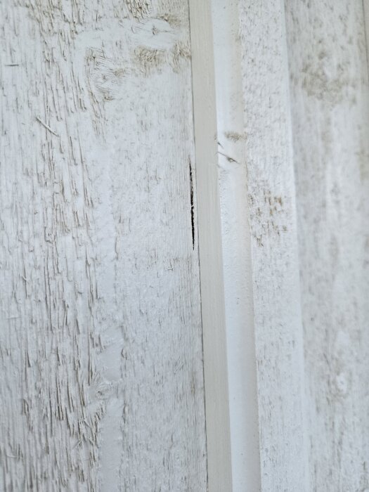 Fasadbräda med synligt spricka och hål i den vita träytan.