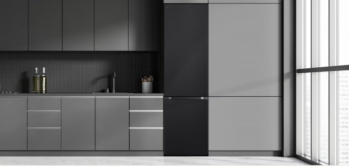 Modernt kök med mörka grå skåp, inbyggd svart kyl och fönster. Kran och diskho syns.
