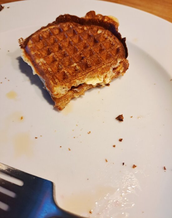 En delvis uppäten våffla på en vit tallrik med några smulor runt om.