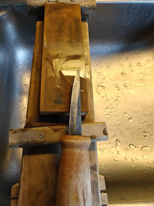 Täljkniv med trähandtag på en slipsten, omgiven av vattenstänk i en diskho.