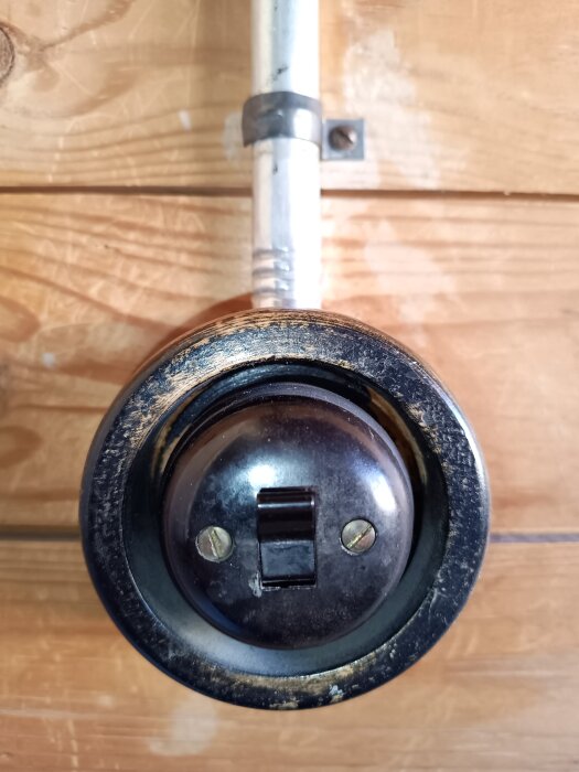 Äldre strömbrytare monterad på trävägg, omgiven av metallrör.