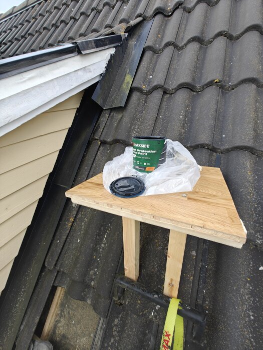 Målad takkupskonstruktion med svart färgburk på träplattform på taket.