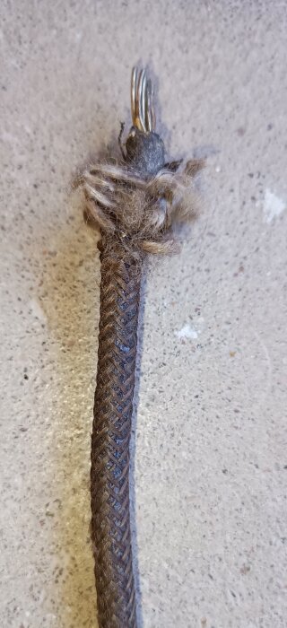 Åldrad isolerad kabel med tjärimpregnerad textil, visar ledningens skick efter 80 år, på betongbakgrund.