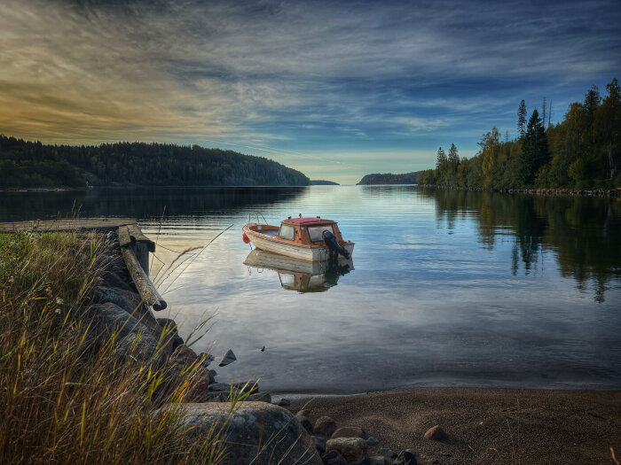 Båt vid Höga kusten i stilla vatten med skogbeklädda stränder under en molnig himmel.