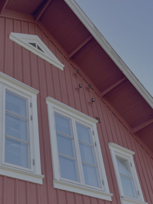 Rödfärgad träfasad med vita fönster och snickeridetaljer; saknar brunglaserat porslinsintag enligt texten.