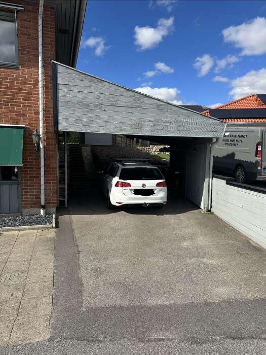 Carport intill hus med asfalt och en parkerad vit bil, diskussion om att konvertera till förråd.