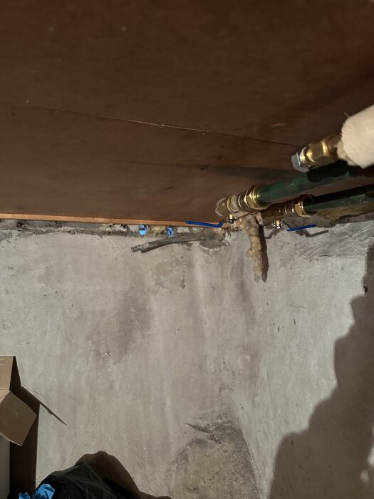 Rör och kopplingar i ett källartak med synliga mässingsfästen och en ventiltapp, fotograferade ovanifrån.