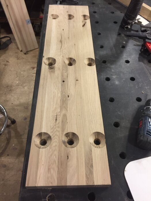 En träskiva med flera ihåliga, frästa cirkulära mönster placerade jämnt på en arbetsbänk i ett snickeri.