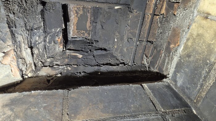 Insidan av en gammal öppen spis med sotig murverk synligt; avsett för installation av en spisinsats.