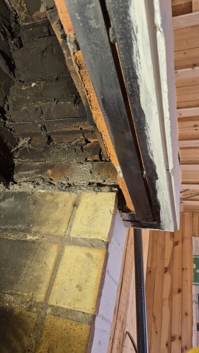 Invändig bild av en gammal öppen spis med tegel och murbruk, samt en kanal upp genom skorstenen. Orange tegel och mörk, sotig yta syns.