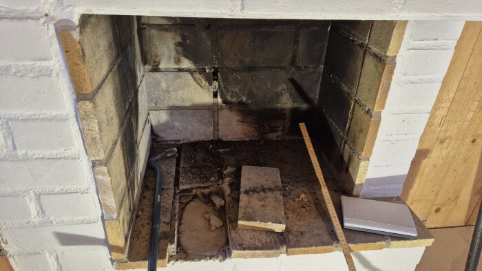 Öppen spis med sotiga inslag, en tegelsten på botten samt ett måttband och ett verktyg placerade på kanten.