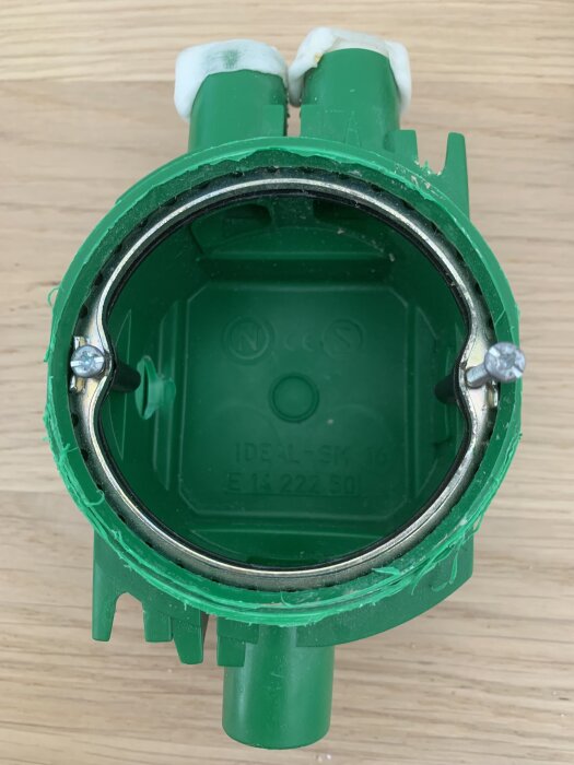 Grön apparatdosa sedd ovanifrån, med två skruvar; en skruv till vänster antas vara icke-standard, de andra två M3.