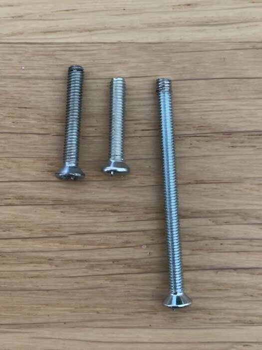 Tre olika skruvar på ett träbord, där den längst till vänster har en avvikande gänga jämfört med de två M3-standard till höger.