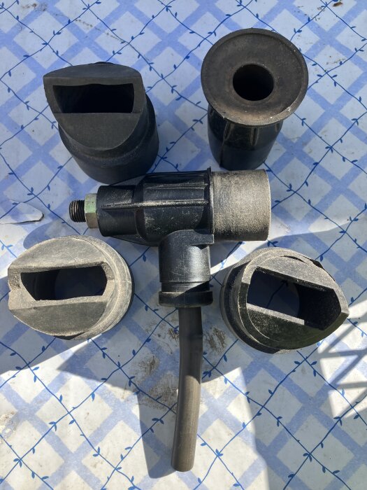 Svart plastdelar i olika former, möjligen verktygstillbehör, placerade på rutigt underlag.