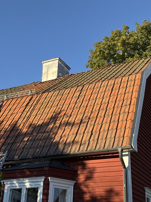 Rött hus med gammalt tegeltak, solen skiner och en skorsten syns. Fråga om tegelpannor för att ersätta taket på ett hus från 1922.