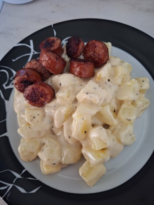 Stuvad potatis med isterband på en svartvit tallrik.