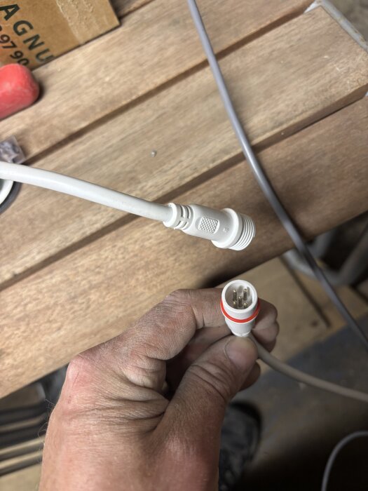 Vit fempolig Balboa-kontakt i en hand, liggande på ett träbord, med texten YVZXF synlig på anslutningen.