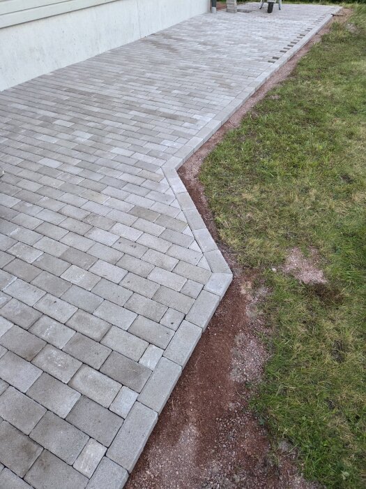 Gård med nylagd stenbroläggning bredvid en gräsmatta, redo för bygget av en entrétrapp och bastu-altan i trä.