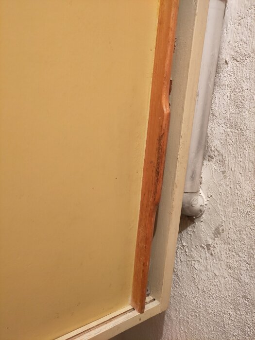 Trädörr i matkällare med brun list för stadga, sedd från sidan. Vägg och rör syns också delvis.