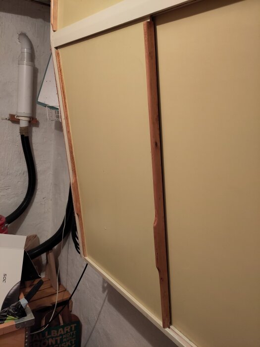 Två skåpluckor med en list för stadga, handtag på båda sidor; en del av ett renoveringsprojekt i en matkällare.