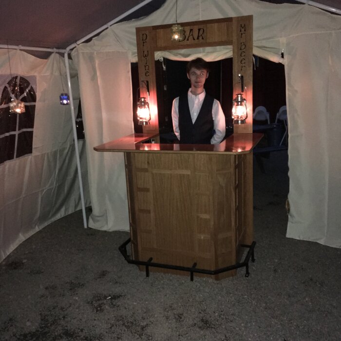 En temporär bar i ett tält med skyltar "Dr Wine" och "Mr Beer" samt en person bakom baren, byggd för en fest.