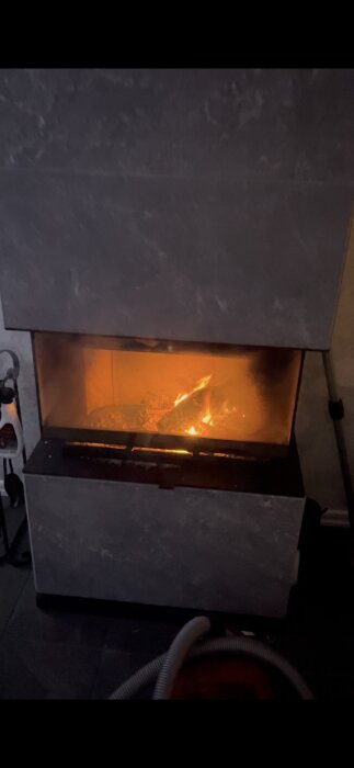 En öppen spis med eld brinnande innanför glasluckor, omgiven av en stenliknande fasad.